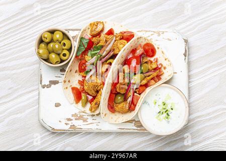 Traditionelles griechisches Gericht Gyros: Pita-Brot mit Gemüse, Fleisch, Kräutern, Oliven auf rustikalem Holzbrett mit Tzatziki-Sauce, Olivenölplatte Stockfoto