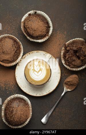 Schokolade und Kakao bräunliche Muffins mit Kaffee Cappuccino in der Tasse von oben auf braunem rustikalem Steinhintergrund, süße hausgemachte dunkle Schokolade Cupcakes, fo Stockfoto