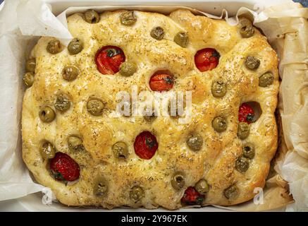 Genießen Sie traditionelles italienisches hausgemachtes Flachbrot Focaccia mit grünen Oliven, Olivenöl, Kirschtomaten und Rosmarin in Backform auf Rustic Dark Stockfoto