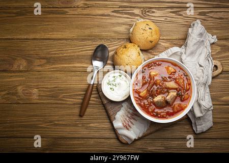 Ukrainische Borscht, rote Rote-Bete-Suppe mit Fleisch, in weißer Schüssel mit Sauerrahm, Knoblauchbrötchen Pampushka und salo-Scheiben auf rustikalem Steinhintergrund. Traditionell Stockfoto