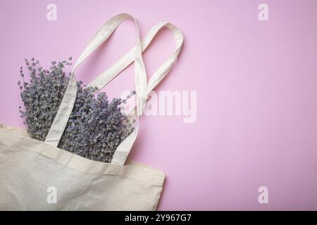 Lavendelblumen-Bouquet in beigefarbener Einkaufstasche aus Öko-Leinen auf violettem Hintergrund, Draufsicht. Romantischer Frühling oder Sommer Mädchen weiblicher Hintergrund, Platz für Stockfoto