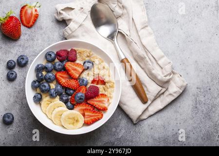 Haferbrei mit Früchten und Beeren in der Schüssel mit Löffel auf weißem Holzhintergrund mit Blick von der Tischplatte, hausgemachtes gesundes Frühstücksflocken mit Strawberr Stockfoto