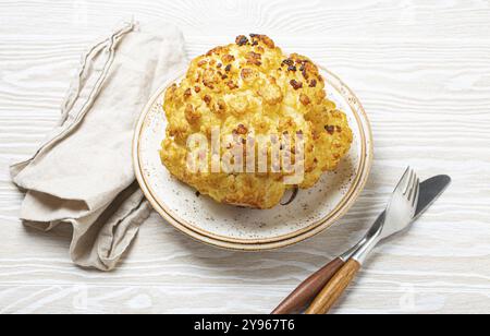 Ganzer gerösteter Blumenkopf mit Olivenöl auf Teller auf weißem hölzernem, rustikalem Tisch mit Besteck. Vegetarisches Gericht, Lebensmittelfotografie, Essen Stockfoto