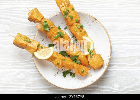 Gegrillte Grilllachsspieße mit grüner Petersilie und Zitrone auf Keramikplatte auf weißem hölzernem rustikalen Tisch Hintergrund von oben Blick, gesundes Essen Stockfoto