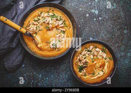 Eine Keramikschüssel mit Kürbiscreme-Suppe, dekoriert mit Erdnüssen auf dunklem Steinhintergrund, mit Löffel von oben dekoriert. Gemütliches Dinner-Konzept im Herbst, s Stockfoto