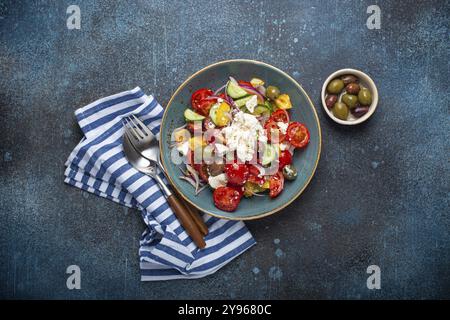 Griechischer frischer, gesunder, farbenfroher Salat mit Fetakäse, Gemüse, Oliven in blauer Keramikschüssel auf rustikalem Betonhintergrund, Draufsicht, mediterrane Würfel Stockfoto