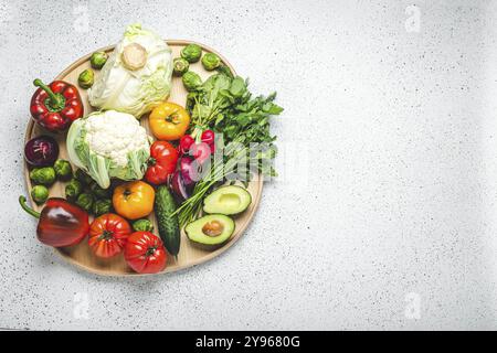 Rustikales Holztablett mit einer Auswahl an frischem Gemüse und Grün auf weißem Küchentisch. Vegetarische oder diätetische Lebensmittel aus ökologischen Zutaten, Stockfoto