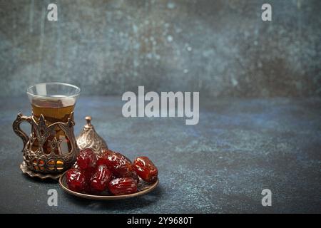 Fastenbrechen mit getrockneten Datteln während des Ramadan Kareem, Iftar-Mahlzeit mit Datteln und arabischem Tee in traditionellem Glas, Blick auf rustikalen blauen Hintergrund Stockfoto