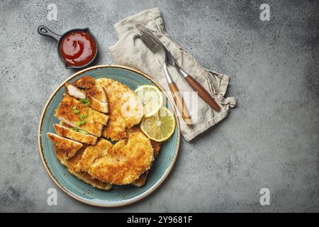 Knuspriges paniertes Hähnchenfilet mit grünem Salat und Zitrone auf einem grauen Tisch mit Ketchup von oben. Japanischer Stil Stockfoto