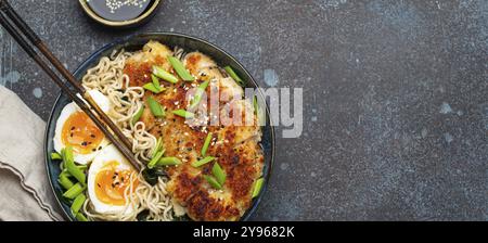 Asiatische Nudeln Ramen-Suppe mit frittiertem Panko-Hähnchenfilet und gekochten Eiern in einer Keramikschüssel mit Koteletts und Sojasauce auf rustikalem Backgroun aus Stein Stockfoto