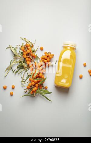 Sanddorn gesundes saftiges Getränk in Flasche und Zweige mit Blättern und Reifen Beeren Top View auf hellgrauem einfachen Hintergrund, Lebensmittelfotografie, Essen Stockfoto