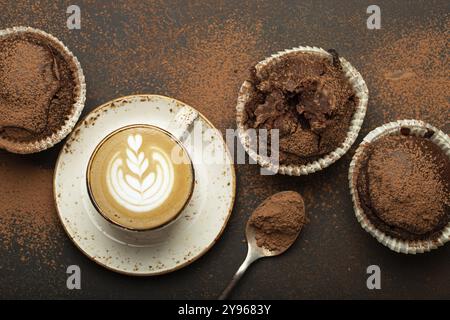 Schokolade und Kakao bräunliche Muffins mit Kaffee Cappuccino in der Tasse von oben auf braunem rustikalem Steinhintergrund, süße hausgemachte dunkle Schokolade Cupcakes, fo Stockfoto