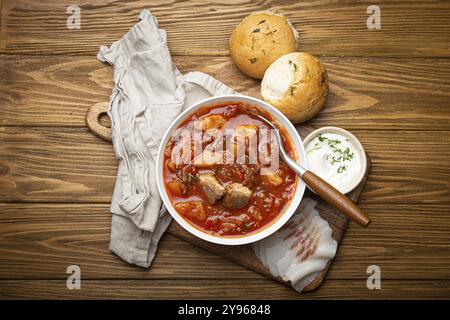 Ukrainische Borscht, rote Rote-Bete-Suppe mit Fleisch, in weißer Schüssel mit Sauerrahm, Knoblauchbrötchen Pampushka und salo-Scheiben auf rustikalem Steinhintergrund. Traditionell Stockfoto