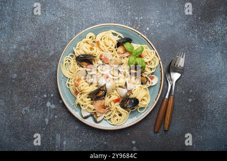 Italienische Meeresfrüchte-Pasta-Spaghetti mit Muscheln, Garnelen, Venusmuscheln in Tomatensoße mit grünem Basilikum auf Teller auf rustikalem blauem Betonhintergrund. Ich Stockfoto