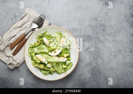 Gesunde grüne Avocadosalatschale mit gekochten Eiern, Gurken, Edamame Bohnen, Olivenöl und Kräutern auf Keramikplatte, Blick von oben auf grauem Stein rustikal Stockfoto