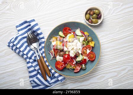 Griechischer frischer, gesunder, farbenfroher Salat mit Fetakäse, Gemüse, Oliven in blauer Keramikschüssel auf rustikalem weißem Holzhintergrund mit Blick von oben, mediterrane Küche Stockfoto