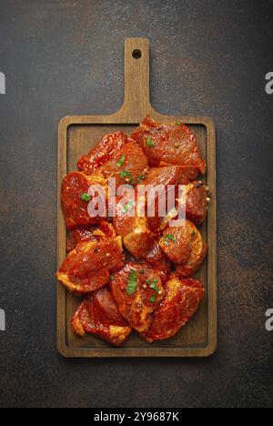 Rohe, ungekochte, geschnittene Schweinefleisch-Stücke, mariniert mit Gewürzen und Petersilie auf hölzernem Schneidebrett von oben auf dunklem rustikalem Hintergrund. Kochen mit Mahlzeit Stockfoto