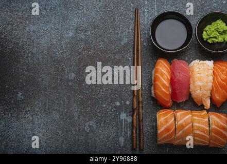 Set aus traditionellem japanischem Sushi und Brötchen mit Blick von oben mit Sojasauce und Essstäbchen auf rustikalem Steinhintergrund. Sushi mit Lachs, Thunfisch und Garnelen, Spa Stockfoto