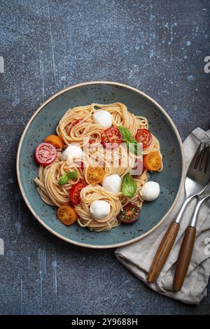 Köstliche Spaghetti mit Mozzarella, farbenfrohe Kirschtomaten, frisches Basilikum auf Keramikplatte auf rustikalem Steinhintergrund mit Blick von oben. Italienisches gesundes Tast Stockfoto