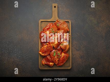 Rohe, ungekochte, geschnittene Schweinefleisch-Stücke, mariniert mit Gewürzen und Petersilie auf hölzernem Schneidebrett von oben auf dunklem rustikalem Hintergrund. Kochen mit Mahlzeit Stockfoto