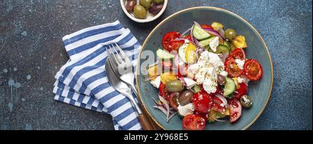 Griechischer frischer, gesunder, farbenfroher Salat mit Fetakäse, Gemüse, Oliven in blauer Keramikschüssel auf rustikalem Betonhintergrund, Draufsicht, mediterrane Würfel Stockfoto