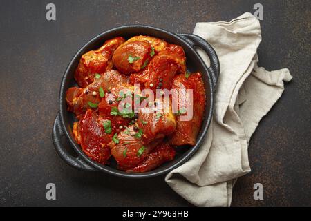 Rohe, ungekochte, gehackte Fleischstücke, mariniert mit Gewürzen und Petersilie in schwarzer Auflaufform, Blick von oben auf dunklem rustikalem Hintergrund. Kochen von Ragouts Stockfoto