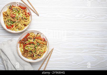 Zwei Schüsseln mit Chow mein oder Lo mein, traditionellen chinesischen Pfannennudeln mit Fleisch und Gemüse, serviert mit Essstäbchen und Blick von oben auf rustikalen weißen wo Stockfoto