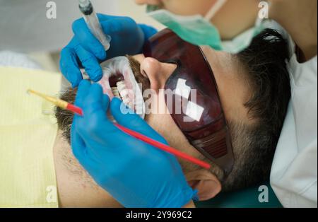 Zahnaufhellung mit ultraviolettem Licht - UV-Lampe. Mann in der Zahnarztpraxis mit Zahnbehandlung. Mann, der beim Zahnarzt die Farbe der Zähne wählt. Stockfoto
