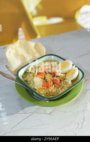 'Traditionelles indonesisches Soto-Gericht mit gekochtem Ei und knusprigen Crackern auf einem hellen Tisch' Stockfoto