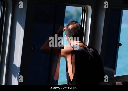 Asiatischer männlicher Passagier, der aus dem Fenster auf einer Fähre über die Inseln in Hongkong blickt Stockfoto