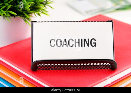 Geschäftskonzept. Der Satz, Text, Wortwahl COACHING ist auf einer weißen Visitenkarte in einem Ständer auf einem Geschäftsnotizbuch geschrieben. Stockfoto