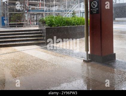 Regen und Hagel auf dem Vorhof eines Gebäudes. Rauchverbot auf der Post. Gerüste um das Gebäude herum zu Wartungszwecken. Stockfoto