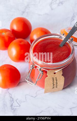 Tomatenpassata in einem Glasklammer-Glas mit Tomaten und einem Löffel beschriftet. Auf weißem Marmorhintergrund Stockfoto