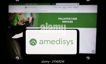 Person mit Smartphone und Logo des US-Gesundheitsunternehmens Amedisys Inc. Auf dem Bildschirm vor der Website. Schwerpunkt auf dem Display des Telefons. Stockfoto