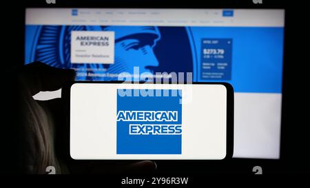 Person, die ein Mobiltelefon mit dem Logo der American Express Company (Amex) auf dem Bildschirm vor der Unternehmenswebseite hält. Schwerpunkt auf dem Display des Telefons. Stockfoto