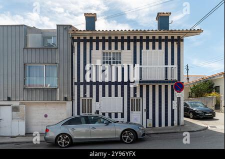 Costa Nova, Portugal - 11. September 2024 : Ein gestreiftes Haus mit Balkon und geparkten Autos in einem Wohngebiet tagsüber Stockfoto