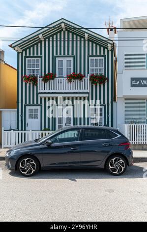 Costa Nova, Portugal - 11. September 2024 : Ein modernes Auto parkt neben einem charmanten gestreiften Haus mit Blumen. Stockfoto