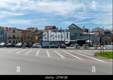 Costa Nova, Portugal - 11. September 2024 : Besucher schlendern in der Nähe von geparkten Autos in einer bezaubernden Küstenstadt unter blauem Himmel. Stockfoto