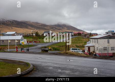 Bakkagerdi, Island, 19.05.2022. Bakkagerdi Stadt im Osten Islands mit traditionellen Wohnhäusern, schneebedeckten Bergen und asphaltierten Straßen. Stockfoto