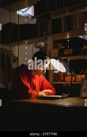 Ein junger Mann liest ein altes Buch in der Bibliothek unter einer Tischlampe. Stockfoto