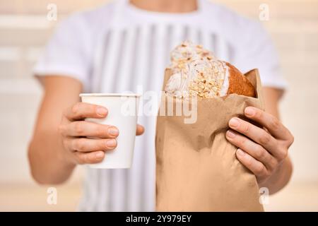 Frau in Schürze serviert dem Gast eine Tasse Kaffee und frisches Croissant aus Papier Stockfoto