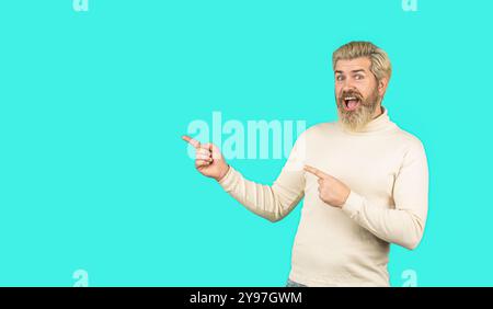 Junger Mann sieht wundert aus und zeigt richtig. Mann mit einem großen Lächeln im Gesicht, der mit der Hand zeigt, mit dem Finger zur Seite. Attraktiver, fröhlicher Mann, der demonstriert Stockfoto