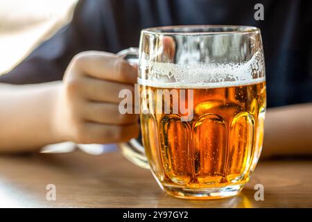 Mann hält Glas mit Bier in einer Bar oder einem Pub, Barkeeper. Nahaufnahme eines Mannes, der ein Glas Bier hält. Hand eines Mannes mit vollem Glas Bier im Pub Stockfoto