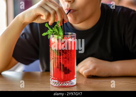 Kind trinkt Erdbeercocktail, Saft mit Minze. Der Junge hält das Glas mit rosafarbenem Cocktail mit Eis und Erdbeerscheibe. Kleiner Junge trinkt Stockfoto