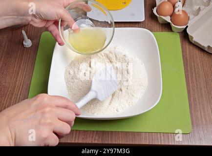 Prozess der Teigherstellung. Frau mischte Puderzucker, Mandelmehl und Eiweiß mit Silikonspachtel in der Schüssel. Macarons zu Hause backen. Nahaufnahme der Hände Stockfoto