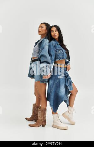 Zwei stylische junge Damen in trendigen Jeansjacken posieren selbstbewusst vor einem schlichten Hintergrund. Stockfoto