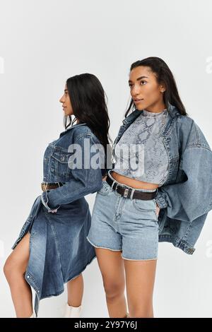 Zwei junge Frauen in modischen Denim-Outfits hocken nebeneinander und strahlen trendiges Selbstvertrauen aus. Stockfoto