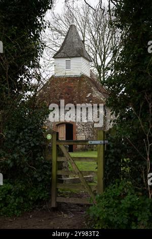 Kleine historische Feuersteinkirche in Alfriston, East Sussex, eingerahmt von Efeu und einem Holztor an einem ruhigen Wintertag im ländlichen England. Stockfoto