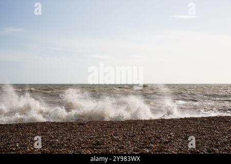 Mächtige Wellen krachen an einem Kiesstrand unter hellem Himmel entlang der Küste des Ärmelkanals, Großbritannien. Stockfoto
