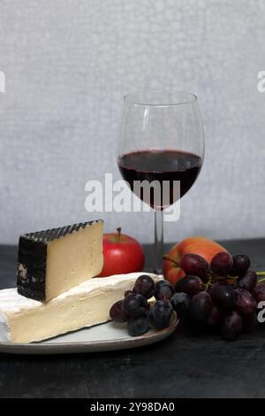 Käseplatte mit Trauben, Rotwein und Apfel auf grauem Hintergrund Stockfoto